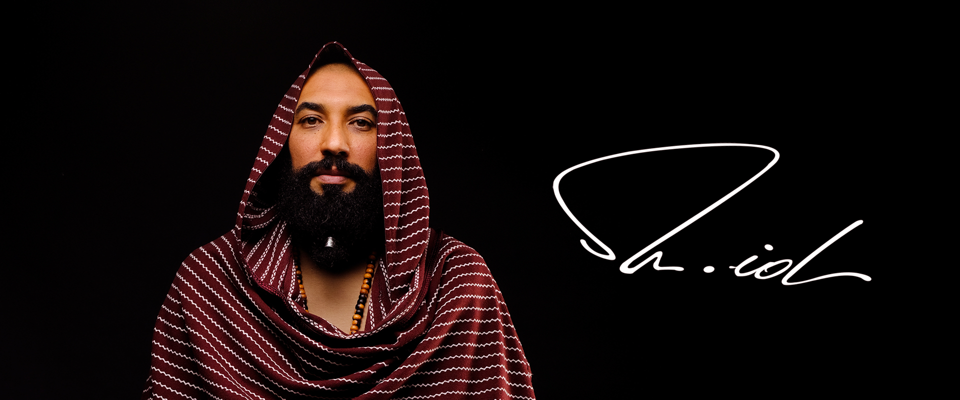 Artista con barba y túnica. Logo del artista a su izquierda.